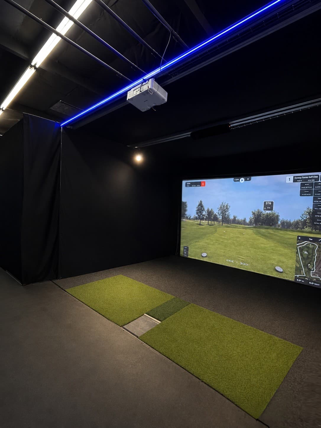 Inside a private simulator bay at Any Swing Golf: hitting mats facing a projected GSPro course on the impact screen